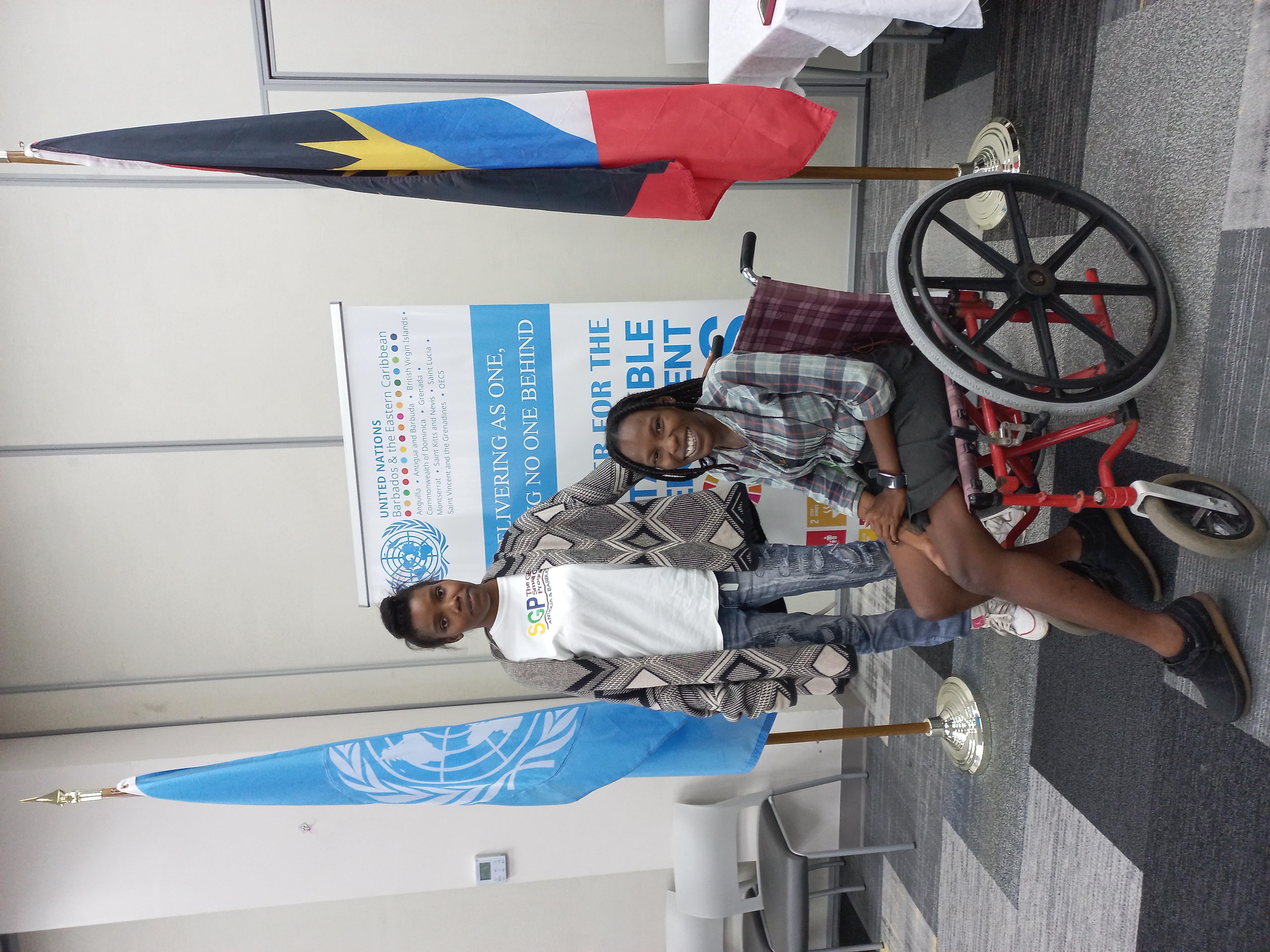 From left to right, Shanika Fedor stands with the support of a walker and Shancia Houston is seated in a wheelchair. The members of the Antigua and Barbuda Association for Persons with Disabilities pose for a photo.